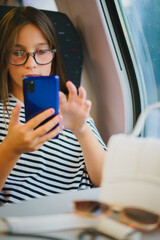 Vertical portrait of girl in glasses travels on train, sits and uses phone