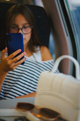 Vertical portrait of girl in glasses travels on train, sits and uses phone
