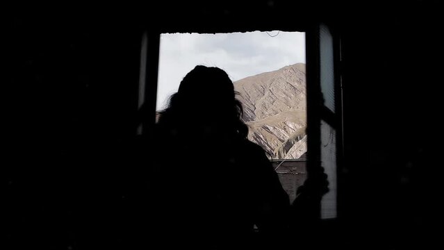 A Woman Opening a Window in Dark Room in Iruya, Salta Province, Argentina.