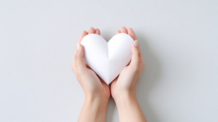 Obraz premium A hand delicately holding a paper heart against a pristine white background. Perfect for conveying heartfelt emotions, this minimalist gesture is ideal for expressing love on various occasions.