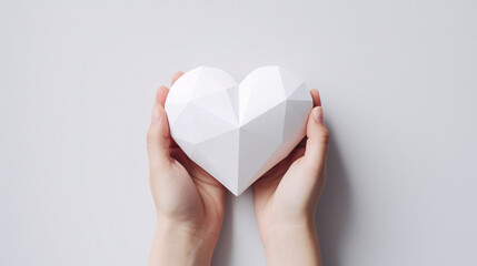 A hand delicately holding a paper heart against a pristine white background. Perfect for conveying heartfelt emotions, this minimalist gesture is ideal for expressing love on various occasions.