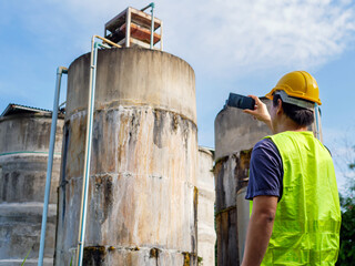 Asian man engineer controlling the quality of water places operating industrial water purification or filtration equipment old cement tanks for keeping water in water factory