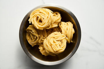 Dry tagliolini or tagliatelle pasta in nests in the bowl on white background. Uncooked ingredient