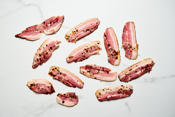 Pancetta slices with spices on white marble background Uncooked and raw. Top view