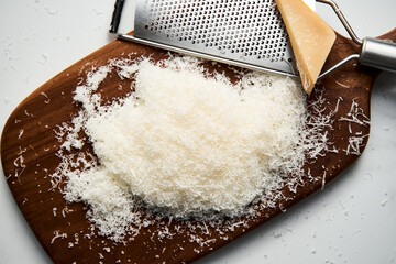 Grated parmesan cheese on a wooden board. White, bright and clean background. - obrazy, fototapety, plakaty