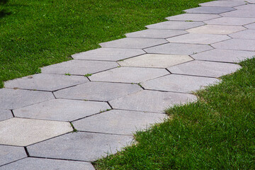 pavement with stone tiles honeycomb pattern on park with green lawn lit by sunlight close-up, nobody.