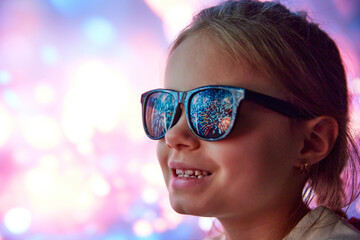 Happy smiling little girl, cheerful child in sunglasses looking on fireworks. Reflection on...