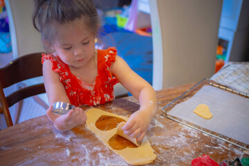 Toddler in red dress makes Christmas cookies with dough