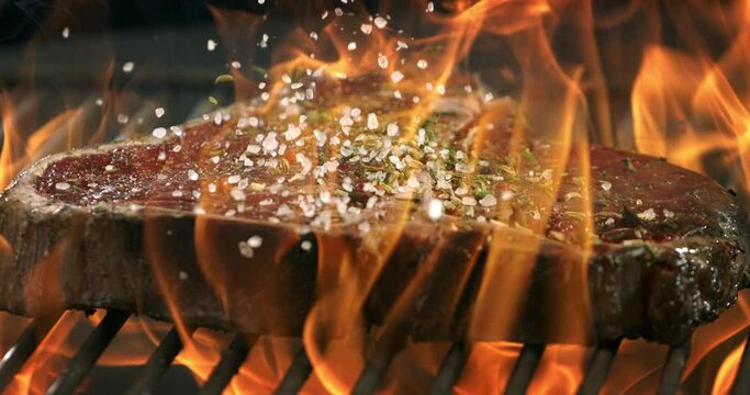 Super slow motion macro of bio juicy beef steak with salt and spices is grilled on grill with open fire by chef in restaurant at 1000 fps.