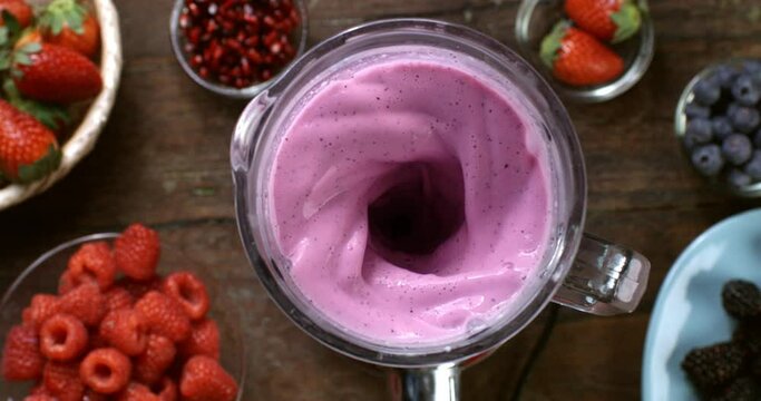 Super slow motion top view of green dietetic milkshake smoothie cocktail of organic fresh berries fruits being mixed in blender at 1000 fps on wooden table of restaurant.