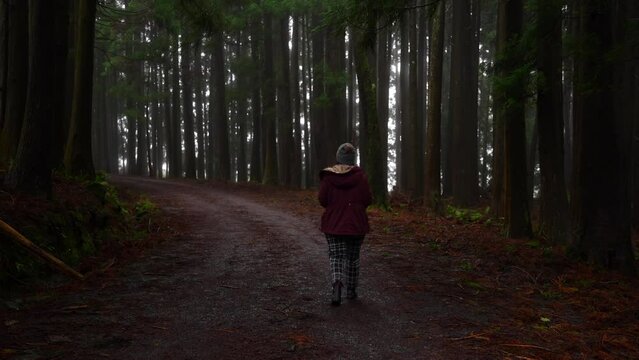 Woman walking through dark forest along path of red volcanic stones in Azores