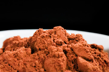 Vista cenital de cacao en polvo en un plato blanco, resaltando su textura rica y color intenso. Ideal para enfatizar ingredientes en repostería y gastronomía.