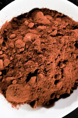 Vista cenital de cacao en polvo en un plato blanco, resaltando su textura rica y color intenso. Ideal para enfatizar ingredientes en repostería y gastronomía.