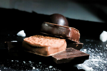 Composición de diferentes tipos de chocolate y bombones sobre una superficie negra, resaltando texturas y colores. Ideal para transmitir la tentación y el placer de los chocolates gourmet.