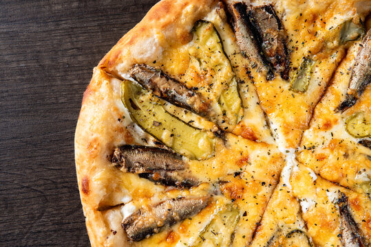 delicious pizza with sprats fish and pickled cucumber on wooden background