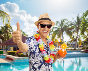 Fototapeta premium Senior tourist holding a cocktail and giving a thumb up by a swimming pool