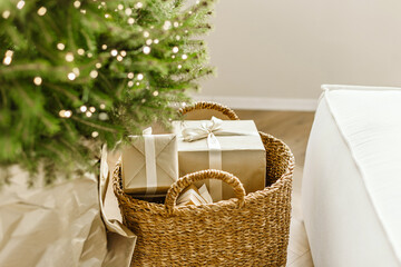 Natural christmas tree pine in wicker bascet with gift boxes in craft paper on wooden floor. Beautiful Christmas tree with gifts and sofa in room, closeup