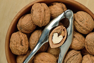 Walnuts in wooden bowl with metal nutcracker and heart shaped walnut