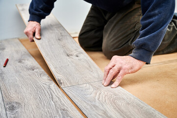 Close up of man construction worker installing laminate timber flooring in apartment under...