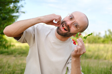 funny young charismatic man in beige t-shirt going to eat delicious ripe red cherries, green garden...