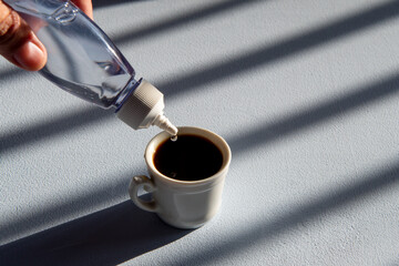 person sweetening coffee with liquid sweetener