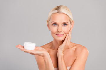Photo of cute pretty old woman naked shoulders applying face cream isolated grey color background