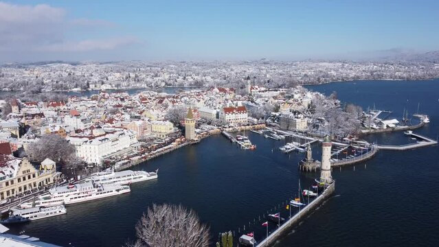Drohnenflug über die märchenhafte Winterinsel Lindau (Bodensee) während der Hafenweihnacht; schneeglänzende Dächer und winterlicher Hafen mit Leuchtturm und Bayerischem Löwen