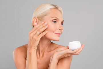 Photo of sweet shiny old woman naked shoulders applying cheeks face lotion isolated grey color...