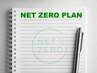 Green text "Net Zero Plan" on the top of blank vertical notepad page with silver pen on white spiral notebook. Climate neutral long term strategy sustainable. Carbon emission net zero goals concepts.
