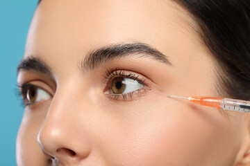 Young woman getting facial injection on light blue background, closeup. Cosmetic surgery