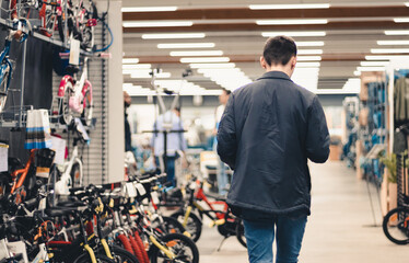 A young man walks down the aisle with bicycle goods in a store.