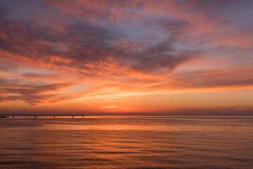 Obraz premium 遠くに桟橋の見える、赤く染まった夕暮れの海と美しい空