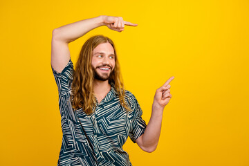 Photo of good mood funky man dressed print shirt pointing two fingers looking empty space isolated...