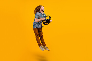 Full length photo of funky cheerful man dressed print shirt driving auto jumping high empty space isolated yellow color background