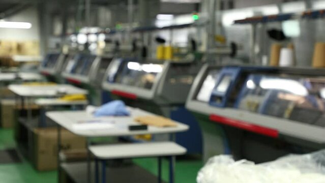 Blurred background view of working knitting machine in workshop. A row of industrial textil flat knitting machines in a knitwear factory. Manufacture of knitwear, modern computerized flat Knitting