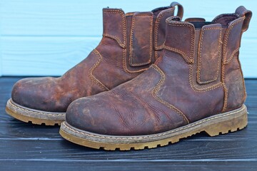 a pair of brown leather old stylish warm winter without laces fashionable with rubber sole comfortable heavy beautiful men's boots stand on a black wooden table