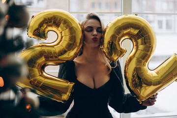 Young blonde woman celebrating her twenty two years birthday and holding figures of numbers 22.