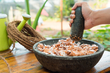 man crushing egg shells with pestle and mortar in a sunny day, and garden as his background, concept of organic fertilizer gardening