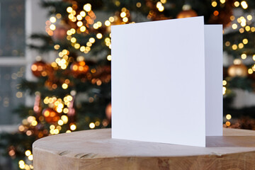 Standing blank empty square greeting card mock up before a blurred christmas tree with copy space....