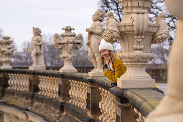Stylish elegant woman in a yellow coat on the steps. Happy female traveler looking at tourist...