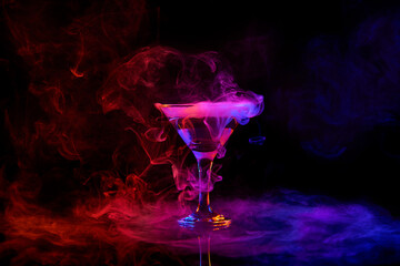 Glass of martini cocktail standing against dark background with neon light with smoke. Traditional...