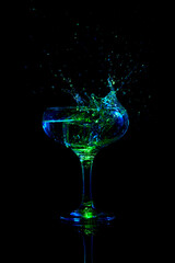 Ice cube falling down into glass with martini cocktail against dark background with neon light. Traditional popular drink. Concept of alcohol drink, nightclub, party, taste, celebration.