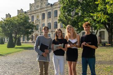 Students with notepads wait for new students near campus. Group of young people needs to meet...