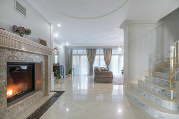 A hall with an exquisite fireplace design and a marble staircase in the interior of a .luxurious...