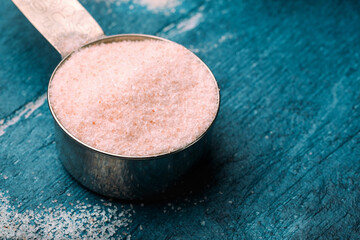 Pink Himalayan salt in measuring spoon on blue wooden background. Selective focus. Toned.