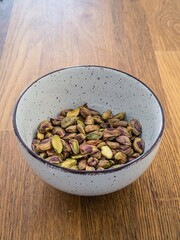Peeled bare naked pistachio nuts in a white bowl on a wooden table