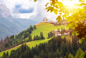 Panoramic view of mountain village with a church in Dolomite alps - obrazy, fototapety, plakaty