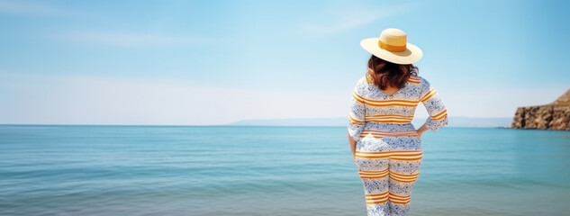 Chubby woman in striped beach suit and straw hat standing by the sea on seashore. Rear view.