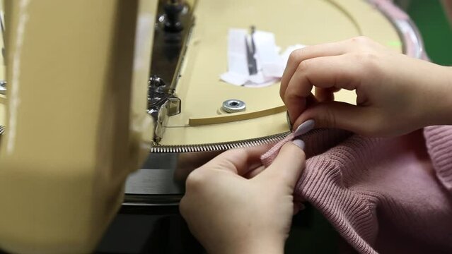 Woman straightens loops on modern automatic knitting machine. Knitter straightens loop on knitted product