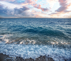 Sea surf. Picturesque seashore with a stone beach at sunset.